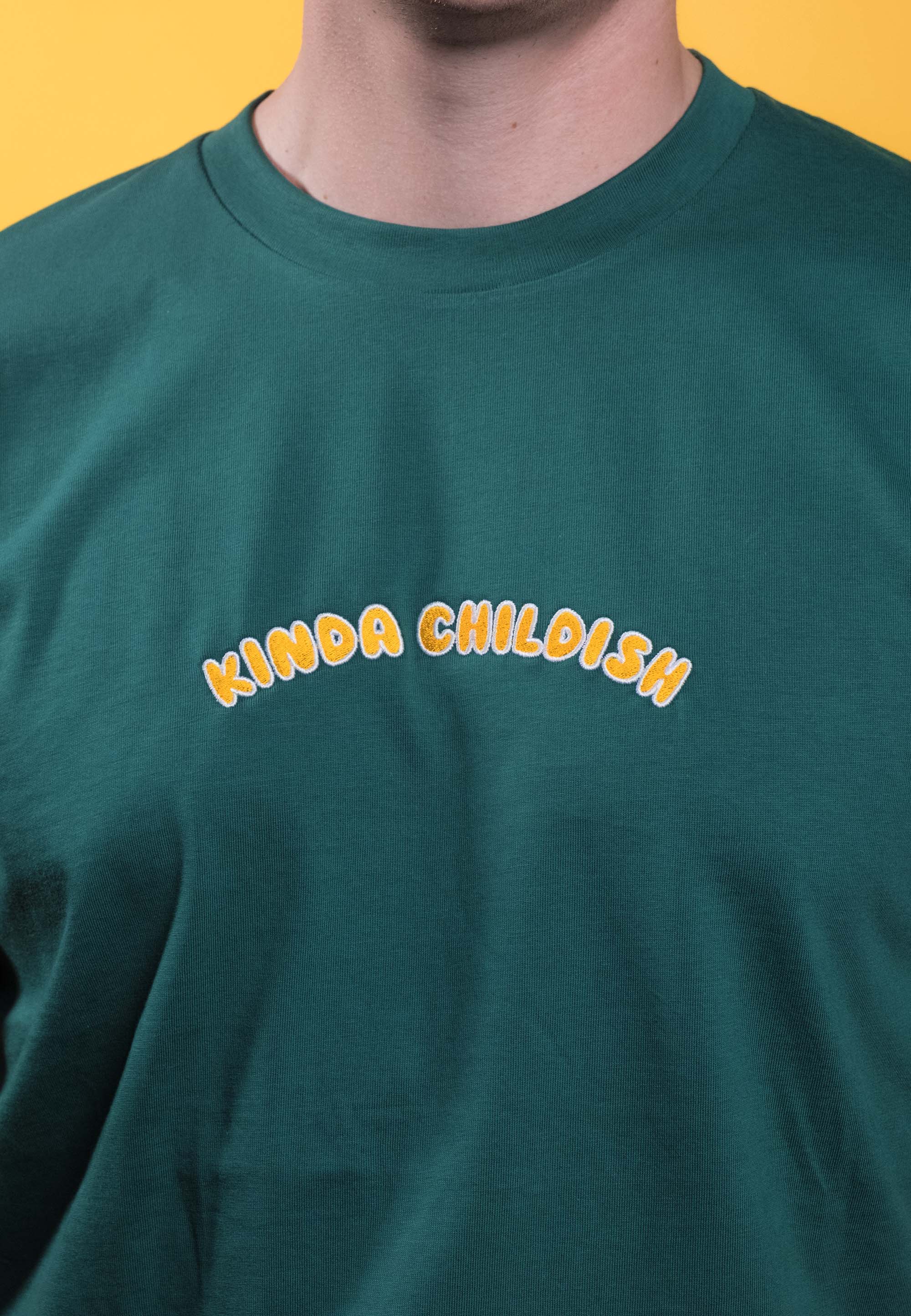 Preshrunk green cotton t-shirt with 'Kinda Childish' embroidered in an arch design
