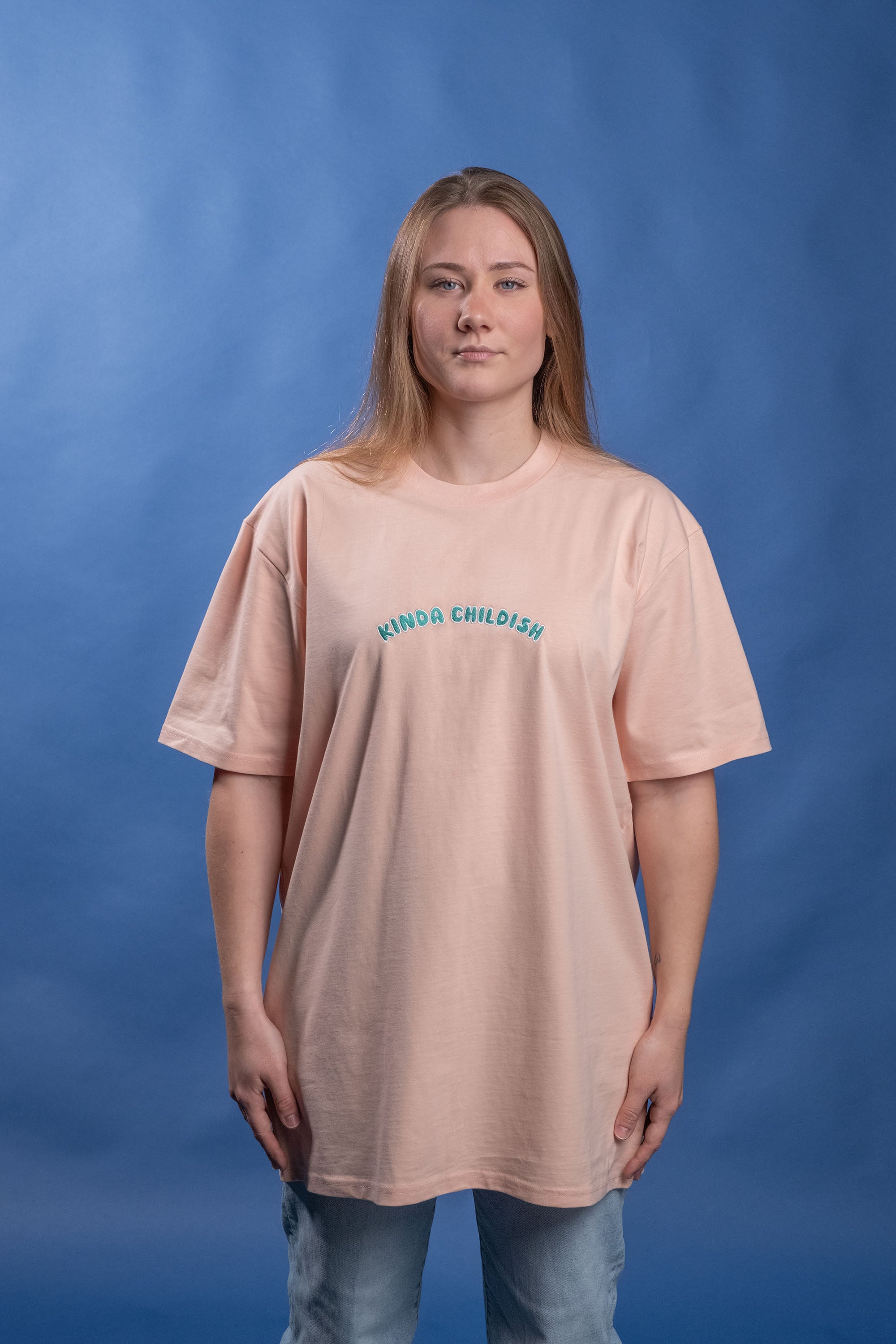 Preshrunk peach cotton t-shirt with 'Kinda Childish' embroidered in an arch design